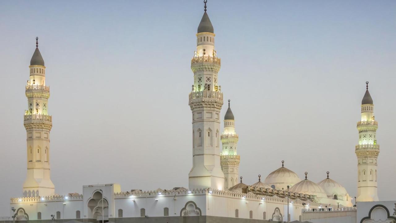 Intercontinental Dar Al Iman Madinah By Ihg Hotel Medina Ngoại thất bức ảnh The image shows a mosque with distinct architectural features, including tall minarets and domes. The minarets are highlighted, likely lit up in the evening, showcasing intricate design elements typical of Islamic architecture. The overall scene conv