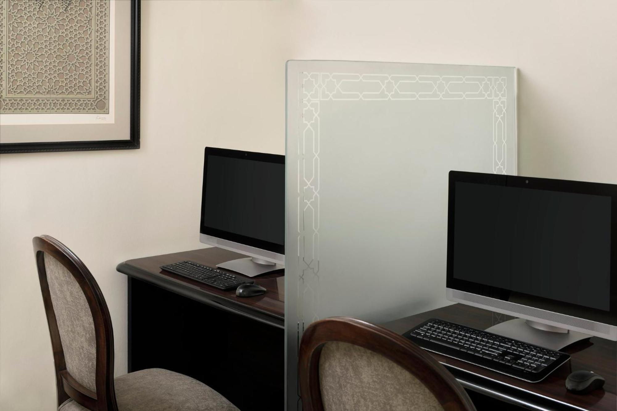 Intercontinental Dar Al Iman Madinah By Ihg Hotel Medina Ngoại thất bức ảnh The photo shows a small office or workspace area featuring two computer stations. Each station has a black monitor, a keyboard, and appears to be set up on a dark wooden desk. A translucent glass partition is placed between the two workstations, prov