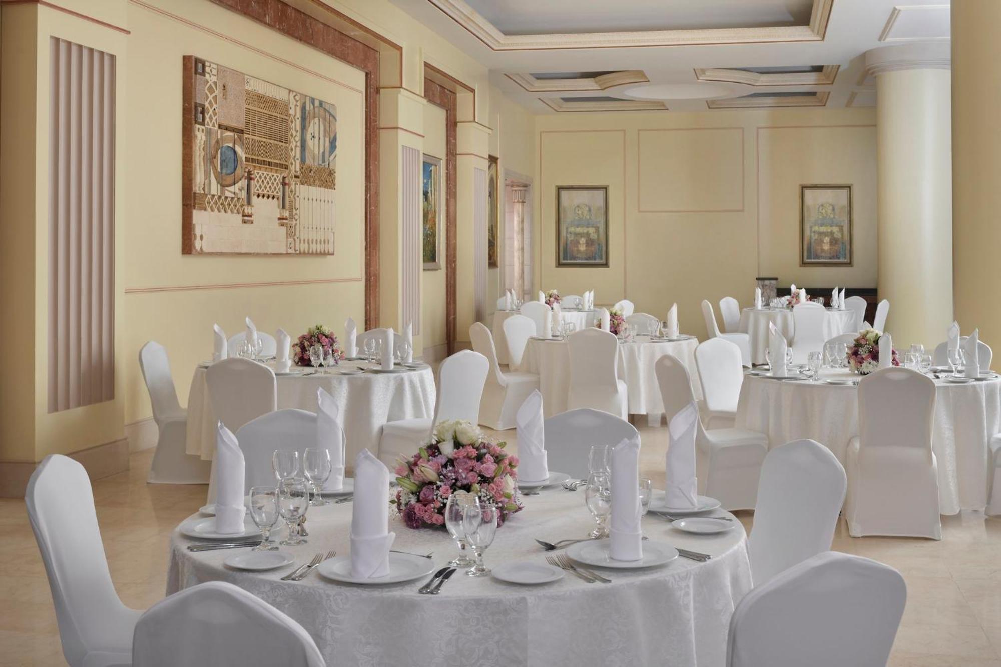 Intercontinental Dar Al Iman Madinah By Ihg Hotel Medina Ngoại thất bức ảnh The photo shows an elegantly arranged dining or function room. There are round tables covered with white tablecloths, each set with fine dining ware including glassware, utensils, and neatly folded white napkins. Some tables have floral centerpieces 