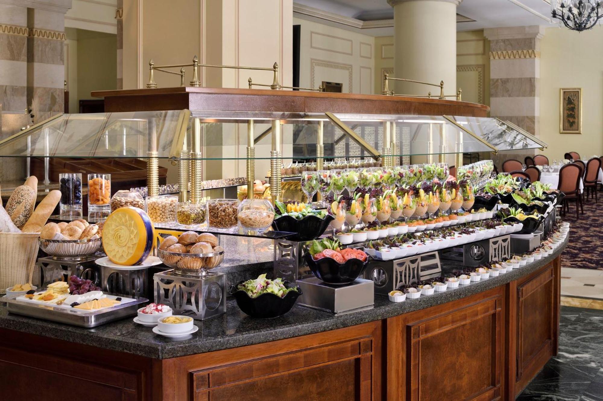 Intercontinental Dar Al Iman Madinah By Ihg Hotel Medina Ngoại thất bức ảnh The photo shows an elegantly arranged buffet with a variety of food items. There is a large, curved wooden display with glass covers, showcasing an assortment of dishes. These include different types of breads and rolls, salads, garnishes, and desser