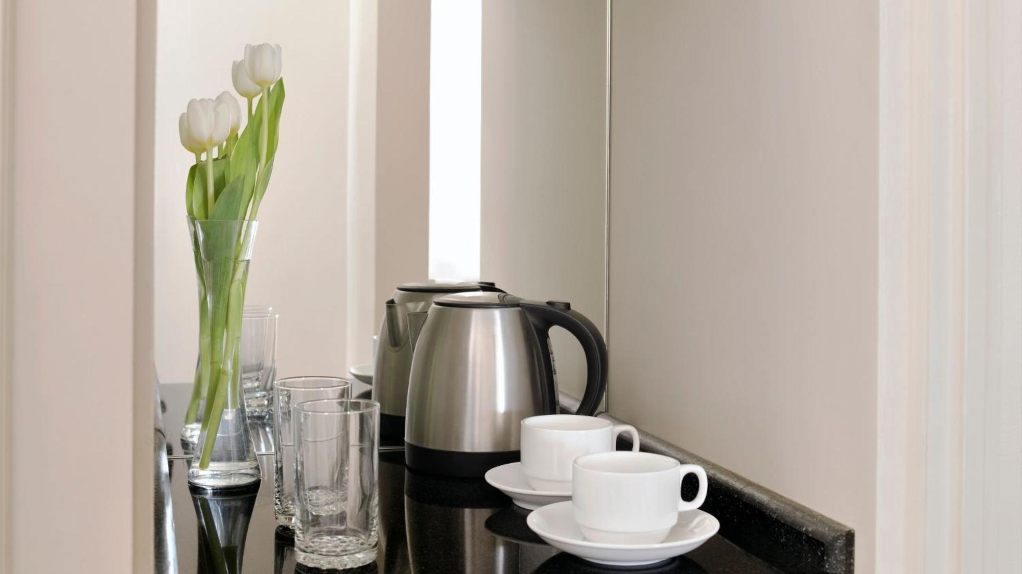 Intercontinental Dar Al Iman Madinah By Ihg Hotel Medina Ngoại thất bức ảnh The photo depicts a neatly arranged beverage area. In the foreground, there are two white coffee cups on small saucers. Next to them, there are two clear drinking glasses. In the background, there is a silver electric kettle, which is positioned next