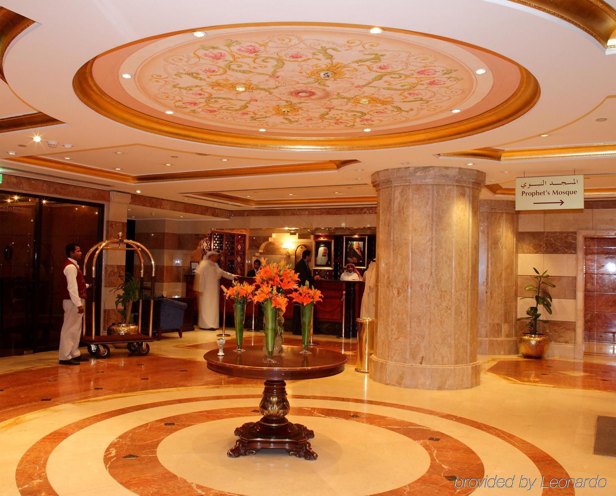 Intercontinental Dar Al Iman Madinah By Ihg Hotel Medina Nội địa bức ảnh The photo depicts a luxurious hotel lobby. The ceiling features an ornate design with floral patterns, adding elegance to the space. In the center of the lobby, there is a decorative table with a bowl or vase of bright orange flowers. The flooring is