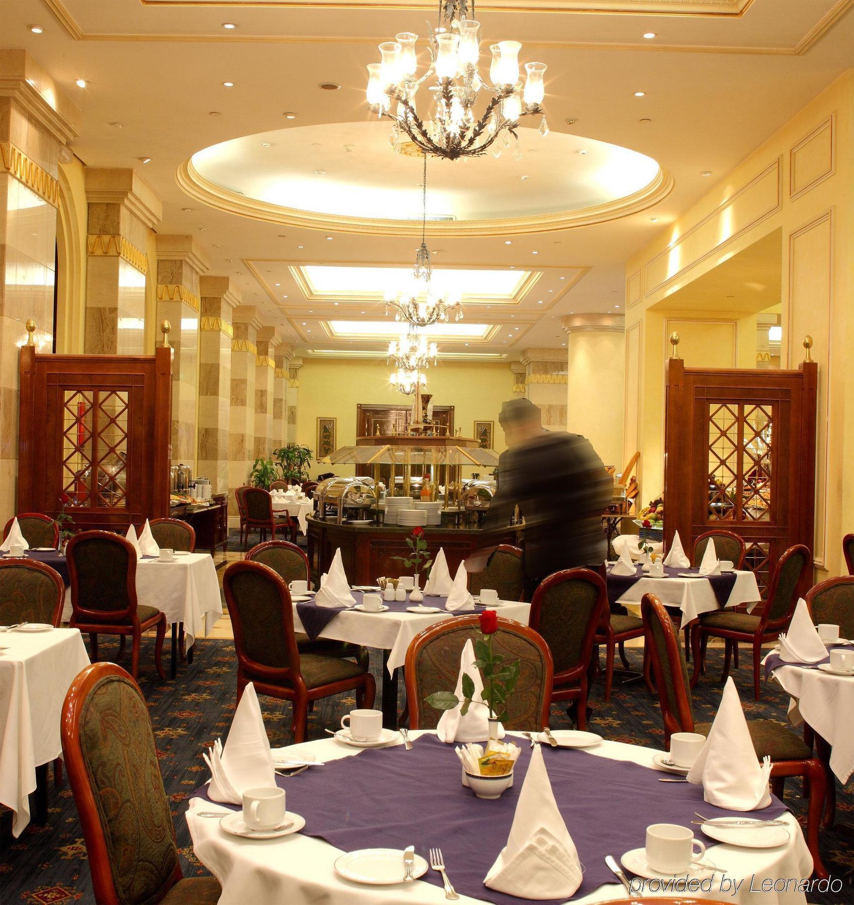 Intercontinental Dar Al Iman Madinah By Ihg Hotel Medina Nhà hàng bức ảnh The photo depicts an elegant restaurant interior. It features round tables covered with white tablecloths, each set with plates, cutlery, and folded napkins arranged into triangles. The space has a warm, inviting atmosphere with a mix of decorative e