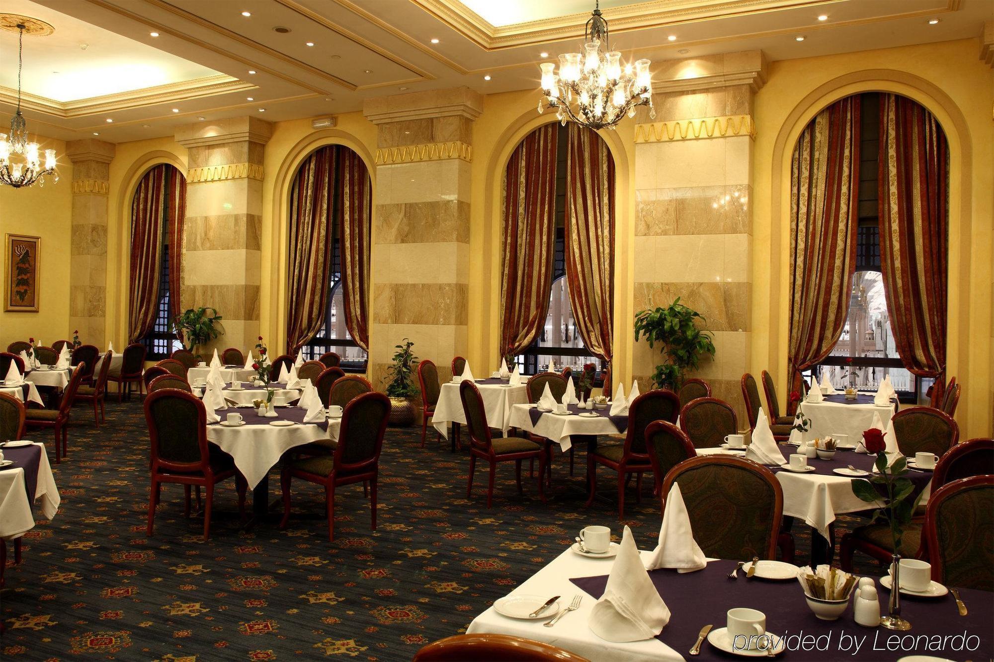 Intercontinental Dar Al Iman Madinah By Ihg Hotel Medina Nhà hàng bức ảnh The photo depicts an elegant restaurant interior. The space features ornate decor with tall windows draped in rich, patterned curtains. Tables are neatly set with white tablecloths and napkins, and there are plush chairs arranged around them. The flo