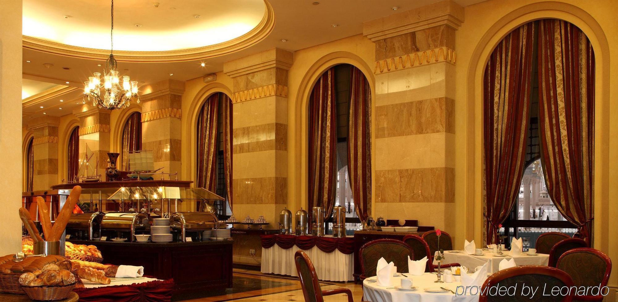 Intercontinental Dar Al Iman Madinah By Ihg Hotel Medina Nhà hàng bức ảnh The photo shows an elegant dining restaurant interior. It features stylish arches and walls with a blend of marble and decorative elements. There are large windows draped with rich curtains, contributing to the luxurious atmosphere. The dining area i