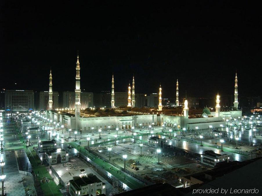 Intercontinental Dar Al Iman Madinah By Ihg Hotel Medina Tiện nghi bức ảnh The image shows the illuminated landscape of a mosque complex at night. It features several tall minarets, which are typically part of Islamic architecture, adorned with lights. The mosque's central building is also brightly lit, surrounded by an ope